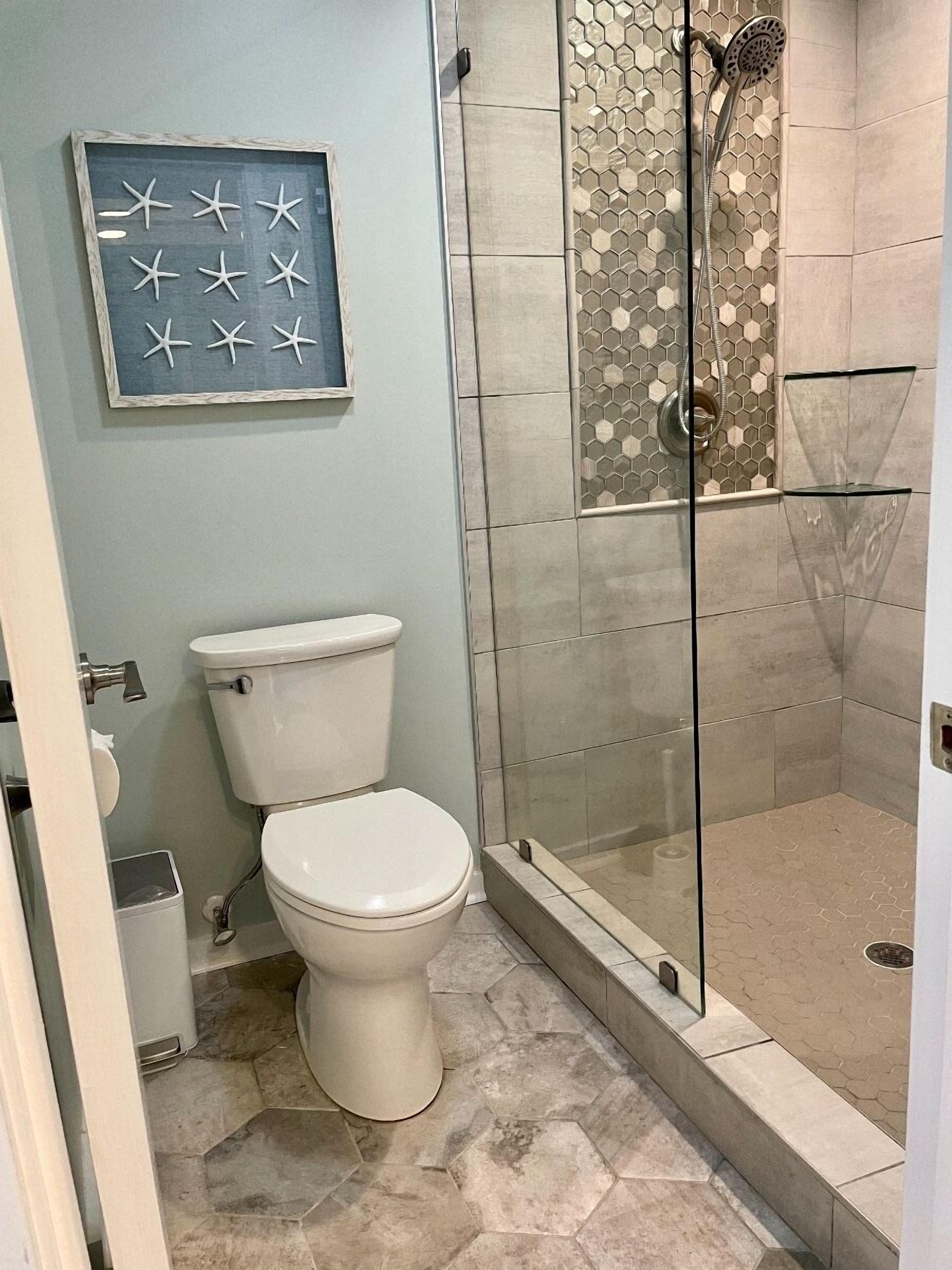 Et badeværelse med toilet, glasvægs brusekabine og en dekorativ vægdekoration.