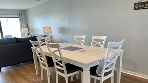 Et spiseområde med et hvidt bord og stole, en grå sofa og en lampe i baggrunden.