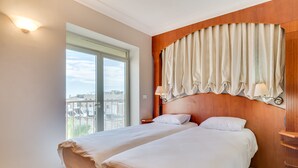 Ein Hotelzimmer mit zwei Betten, einem großen Fenster und Blick auf die Stadt.