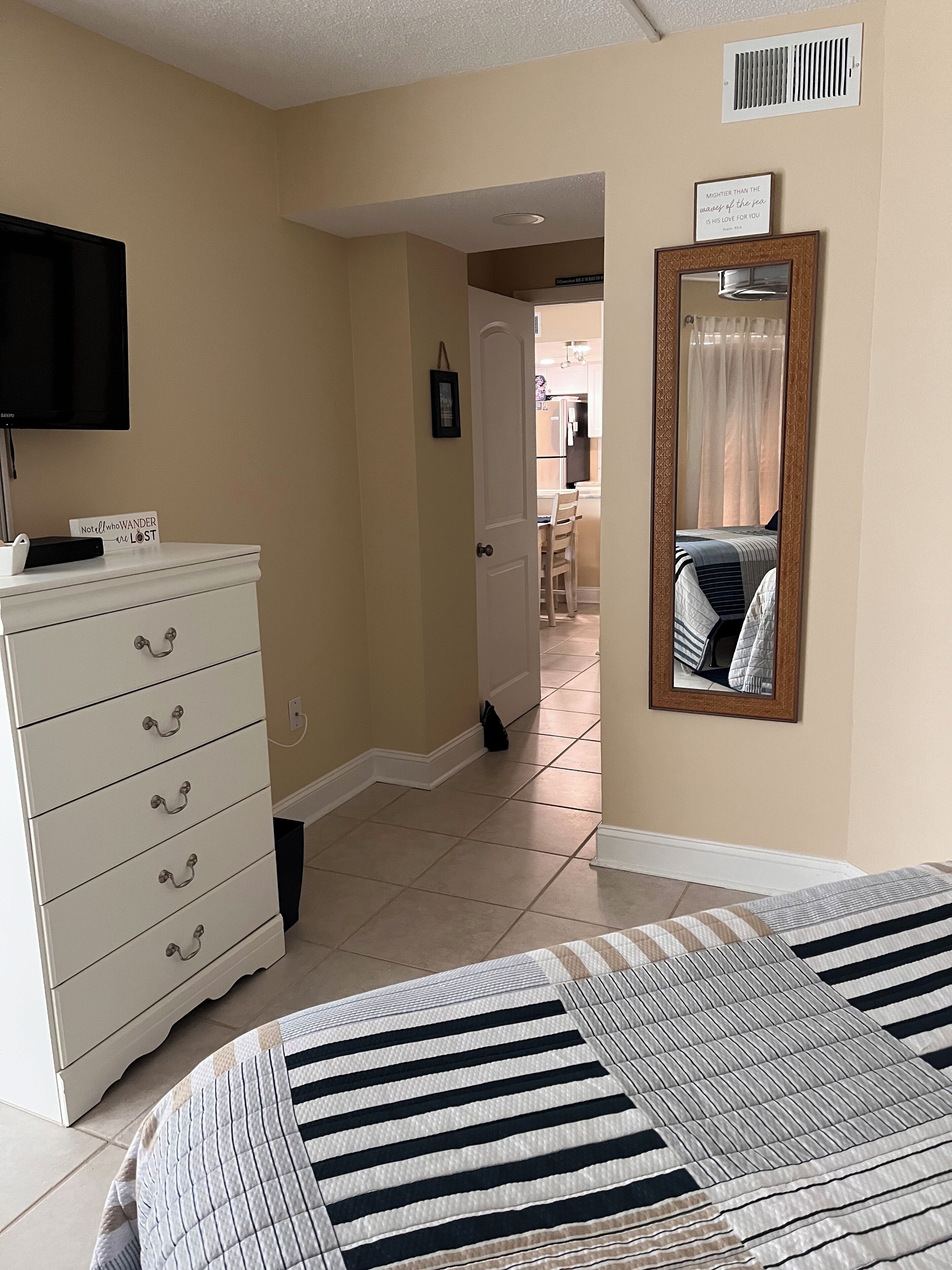 A bedroom with a bed, a dresser, a television, and a mirror.