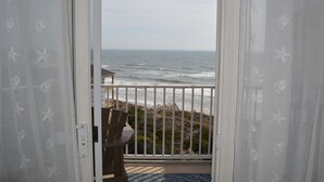 Vue depuis un balcon doté d’une balustrade blanche, donnant sur l’océan et la plage.