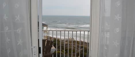 Vista desde un balcón con barandilla blanca, con vista al océano y la playa.