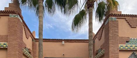 A building with a tiled entrance, palm trees, and a patterned walkway.