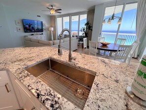 Enjoy ocean views from the spacious living area, featuring a dining table for four, a large flat-screen TV, and a modern kitchen with a stainless steel sink.