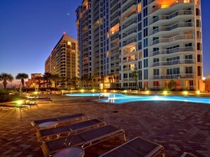 Relax by the rectangular pool surrounded by lounge chairs and tables, with hotel rooms offering stunning views.