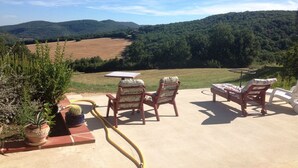 An outdoor patio with two wooden chairs and a table, overlooking a scenic landscape with hills and a field. - Domaine du Colombier- A Southern France Living Experience (Larroque)