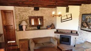 A cozy living room with a stone wall, a fireplace, a sofa, a wooden cabinet, and a tiled floor. - Domaine du Colombier- A Southern France Living Experience (Larroque)