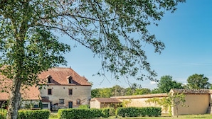 A rustic outdoor seating area with wicker furniture and a stone table, surrounded by a well-maintained lawn and a large building with a tiled roof. - Château des Louteaux (Chézy)