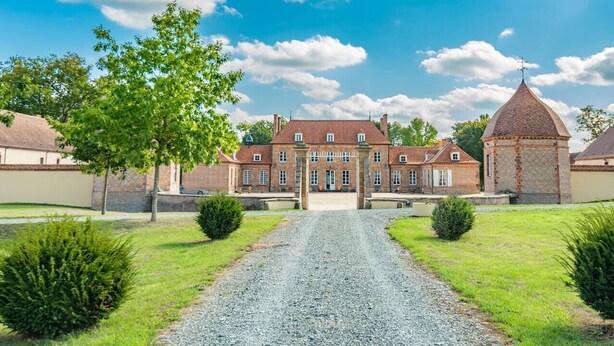 A large, historic building with a central courtyard, surrounded by well-maintained lawns and a gravel path leading to the entrance. - Château des Louteaux (Chézy)