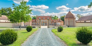 Un grand bâtiment historique doté d’une cour intérieure, entouré de pelouses bien entretenues et d’un chemin de gravier menant à l’entrée.
