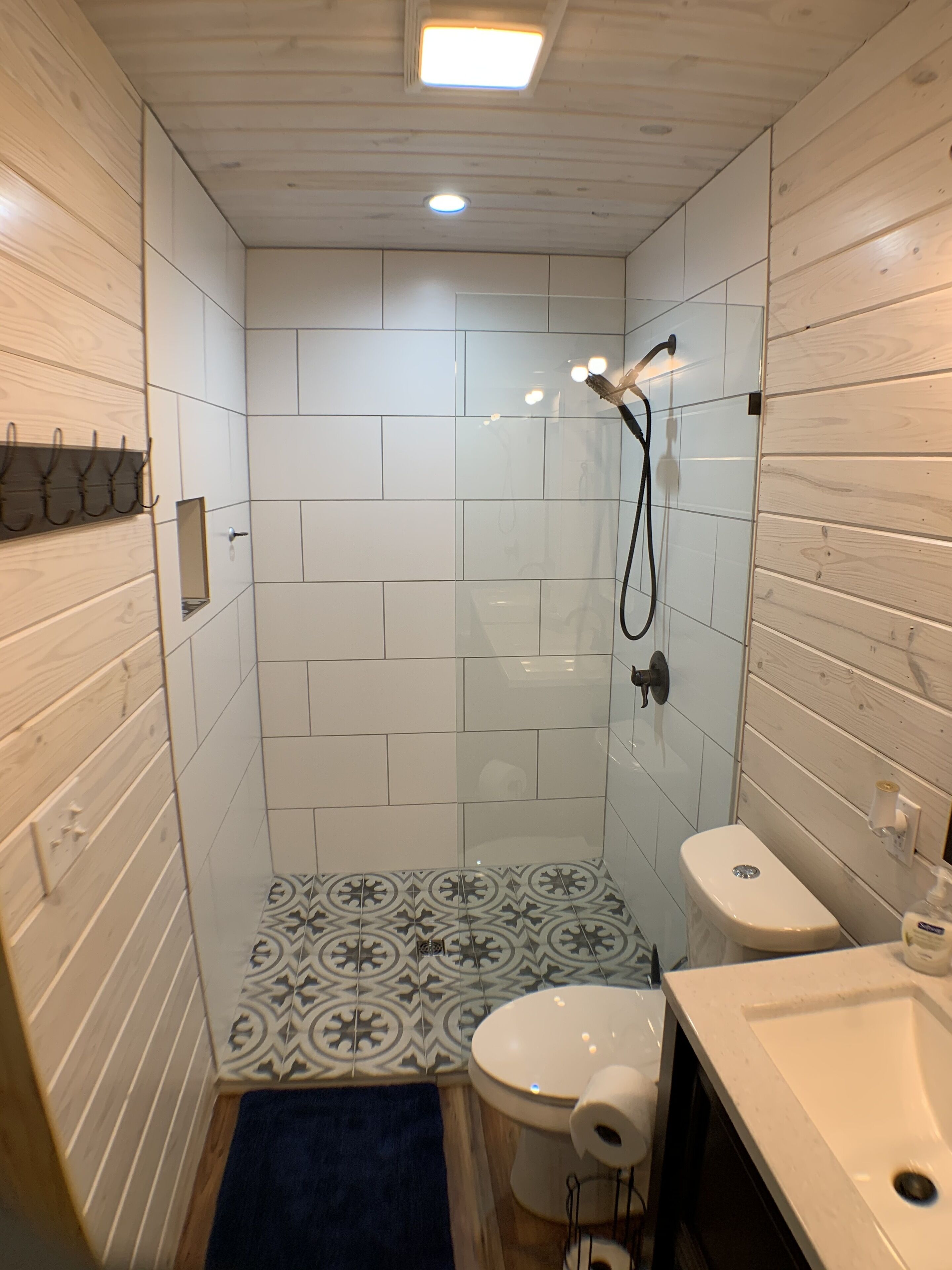 Un baño pequeño y moderno con azulejos blancos, ducha, inodoro y lavamanos.