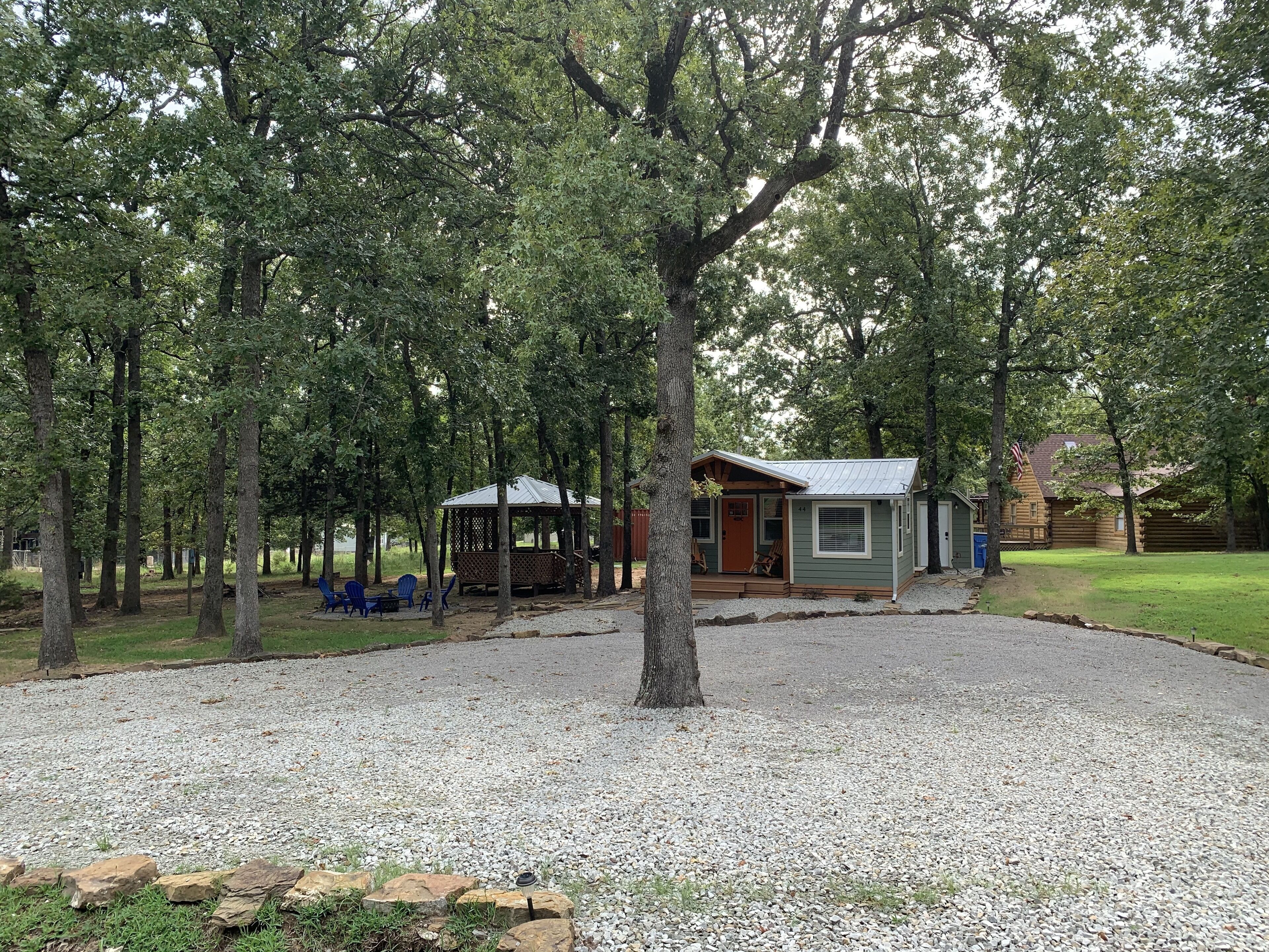 A rustic cabin with a porch, surrounded by trees and a gravel driveway.