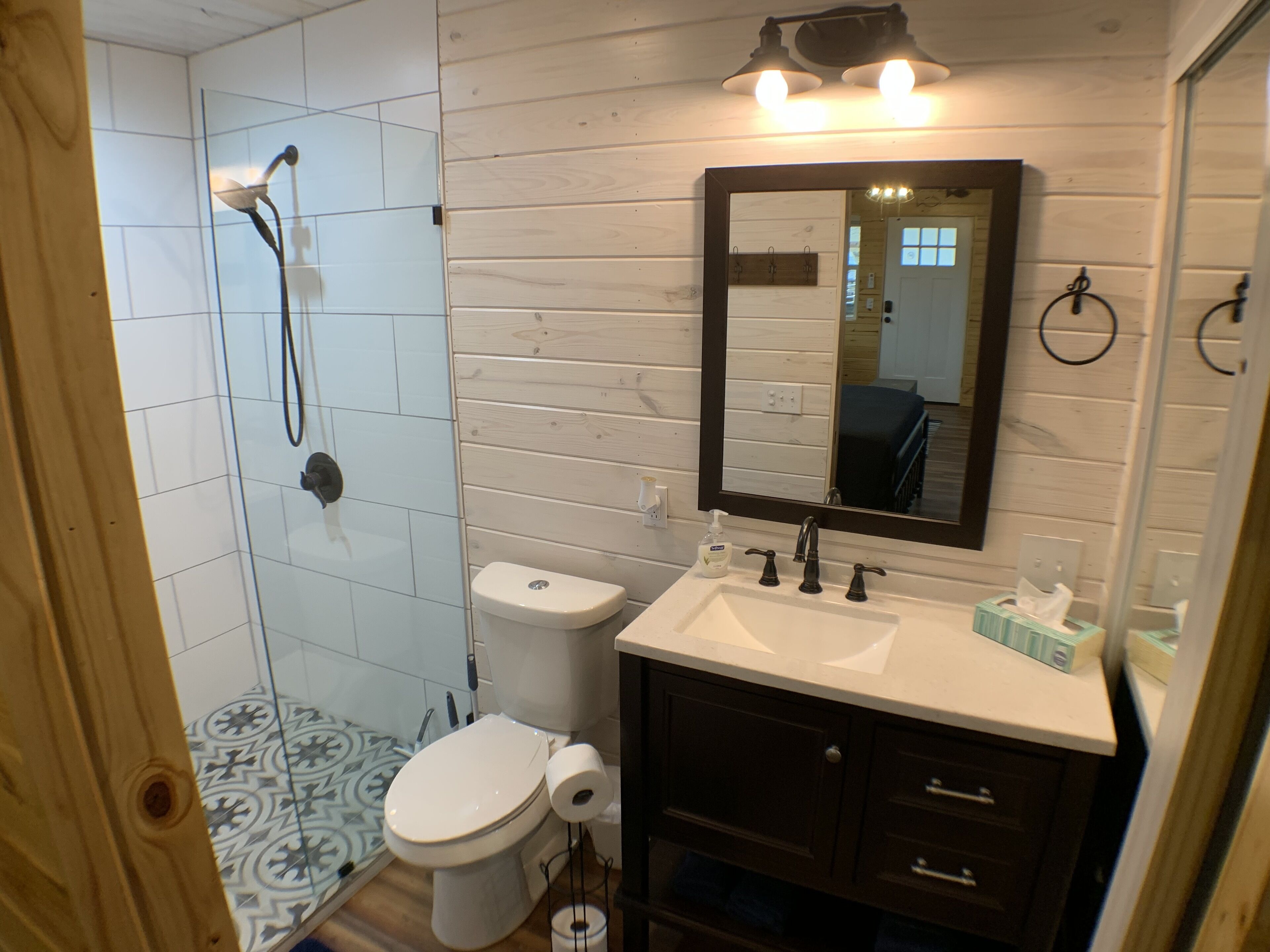 A bathroom with a shower, toilet, sink, and mirror.