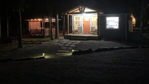 Pieni, viihtyisä mökki, jossa on kuisti ja keinutuolit, ja sen ympärillä kasvaa puita.