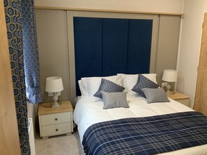 A bedroom with a bed, two bedside tables with lamps, a blue headboard, and patterned curtains.