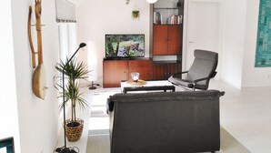 A modern living room with a sofa, a television, a bookshelf, and a potted plant.