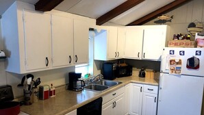Eine Küche mit weißen Schränken, einem schwarzen Geschirrspüler, einem weißen Kühlschrank und einer Kaffeemaschine.