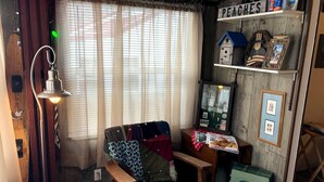 Ein gemütliches Zimmer mit einem Holzstuhl, einem kleinen Tisch mit Lampe, einem Regal mit Dekorationen und einem Fenster mit Vorhängen.