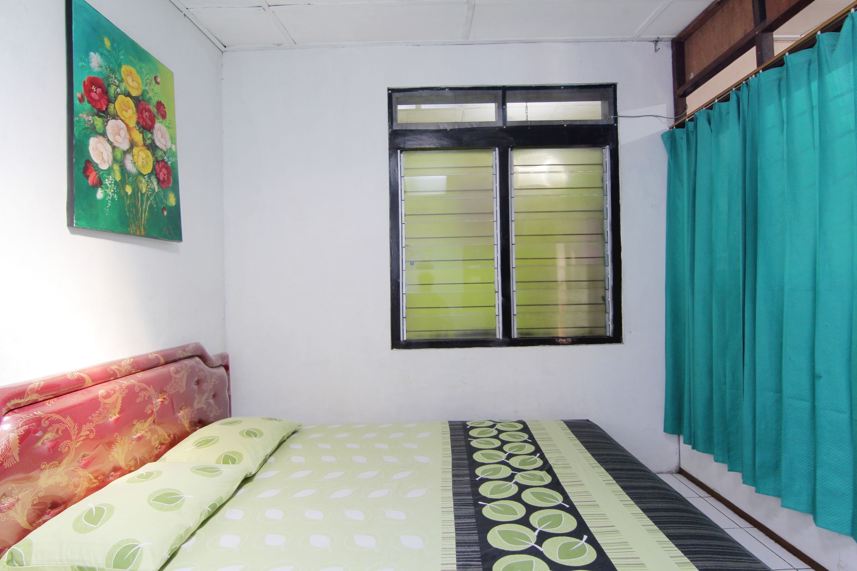 A room with a bed, a window with curtains, and a wall with a floral painting.