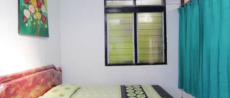 A room with a bed, a window with curtains, and a wall with a floral painting.
