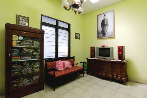 A room with a wooden cabinet, a sofa with a pink cushion, a television, and framed pictures on the wall. - Batik Trinidar Homestay by Zuzu (Yogyakarta)