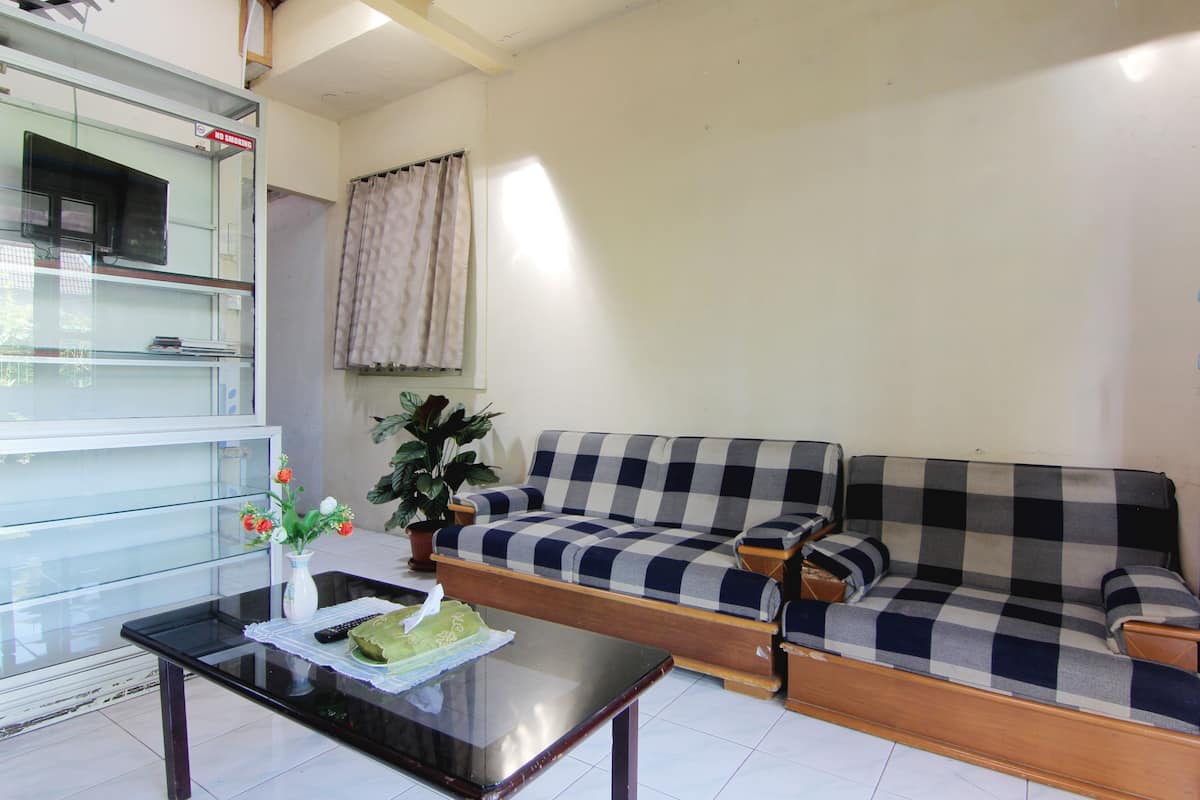 A living room with a checkered sofa, a glass cabinet, a small table with a vase of flowers, and a potted plant.