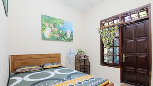 A bedroom with a bed, a window with curtains, a door, and a wall-mounted fan. - Batik Trinidar Homestay by Zuzu (Yogyakarta)