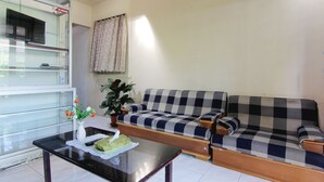 Una sala de estar con un sofá a cuadros, una mesa de centro de vidrio, un televisor y una planta en maceta.