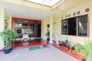 A hotel entrance with a red tiled floor, a covered entrance area, and potted plants. - Batik Trinidar Homestay by Zuzu (Yogyakarta)