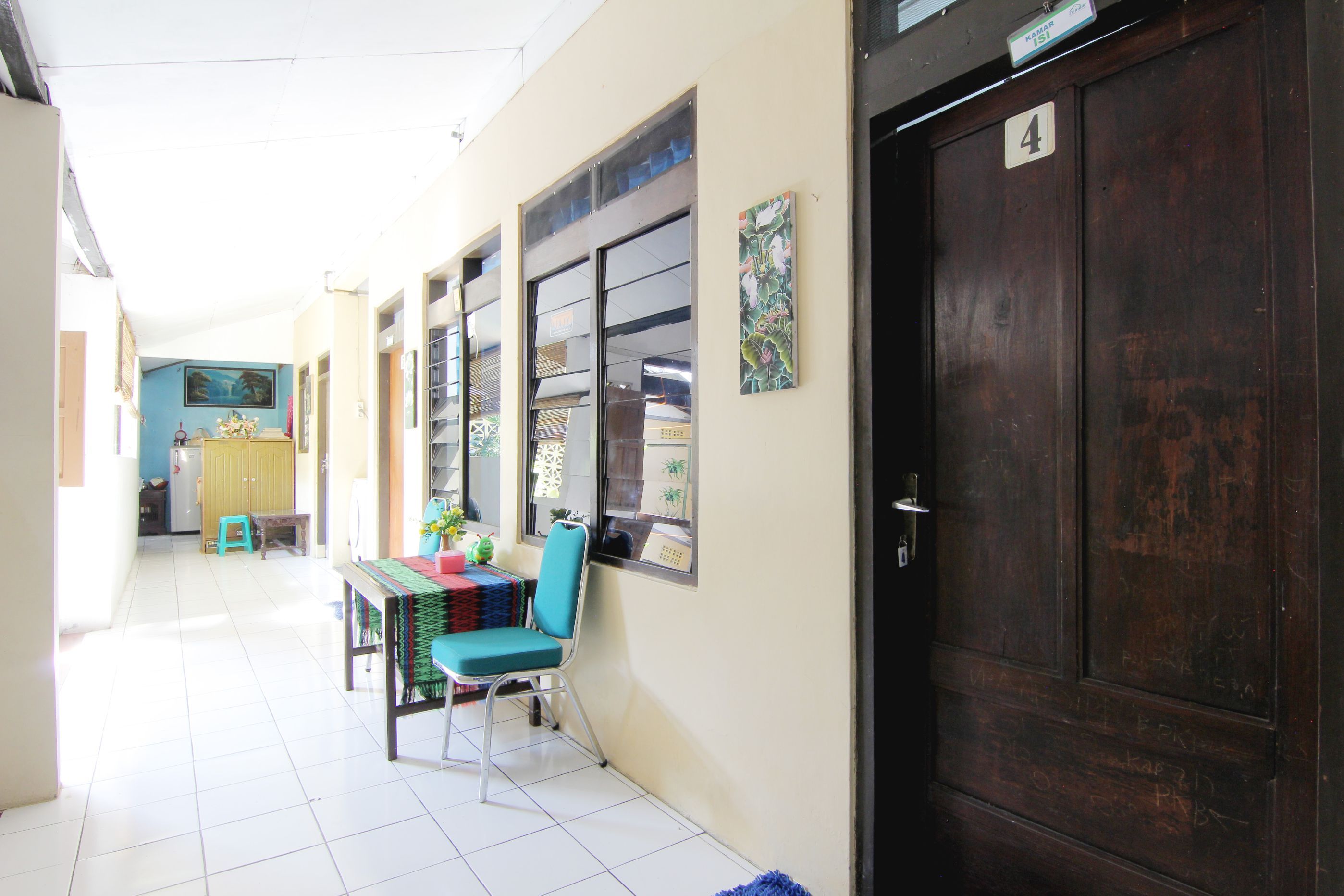A hallway with a closed wooden door, a tiled floor, a table with chairs, and a window with a view of the outside.