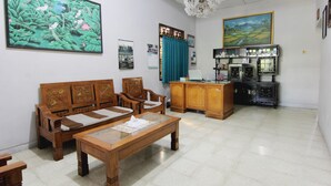 Una habitación con un sofá de madera, una mesita de centro, un mueble con vajillas de té y un cuadro en la pared.