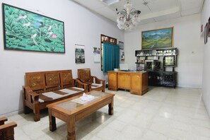 A living room with a wooden sofa, a coffee table, and a cabinet with glassware. - Batik Trinidar Homestay by Zuzu (Yogyakarta)