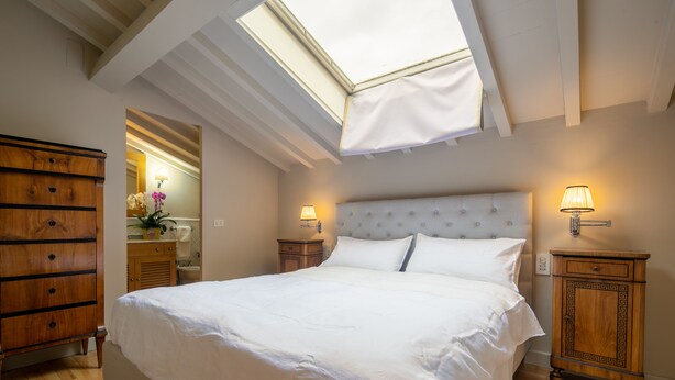 A bedroom with a skylight, a bed with white linens, two bedside tables with lamps, and a wooden dresser. - San Jacopo Top by Mmega (Florence)