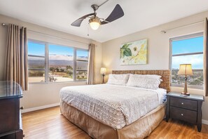 Un dormitorio con una cama grande, un ventilador de techo, dos lámparas de noche y vistas a la ciudad a través de amplios ventanales.