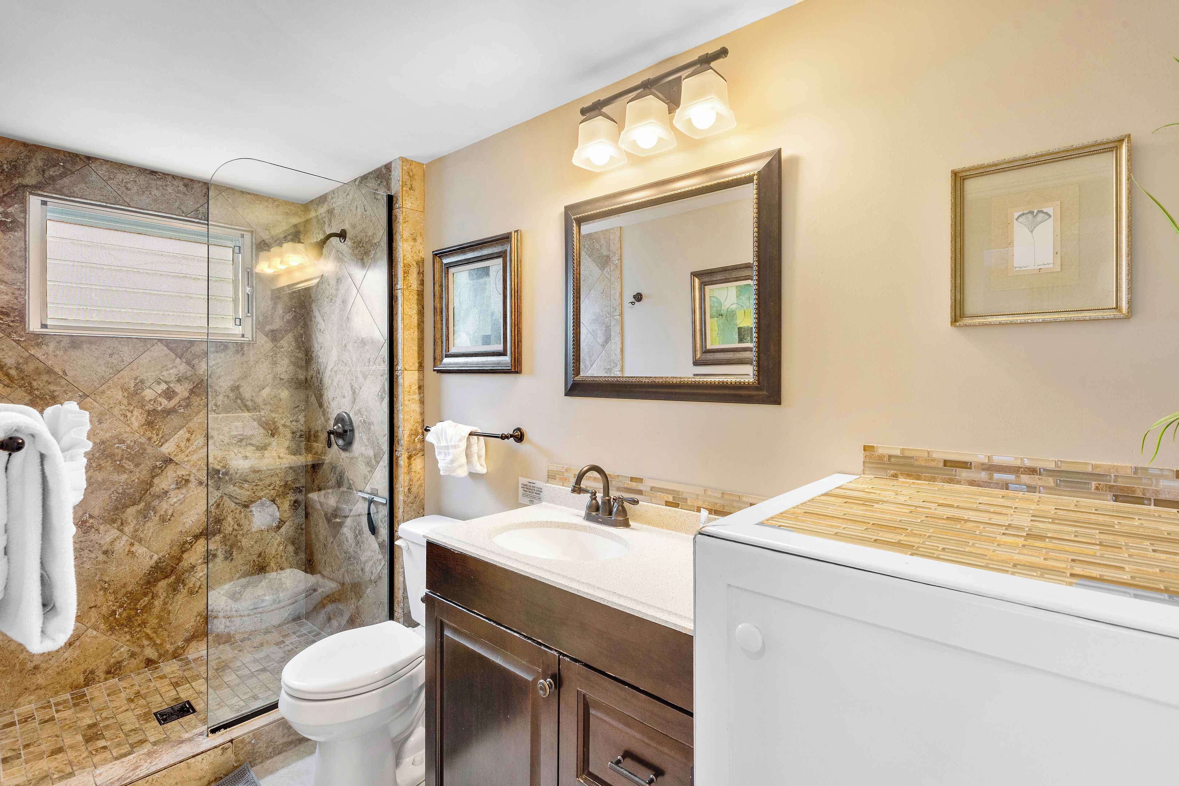 A bathroom with a glass shower enclosure, a white sink, and a vanity with a mirror.