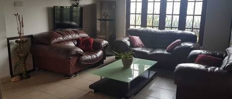 Un salón con dos sofás de cuero, una mesa de centro de vidrio y un televisor.