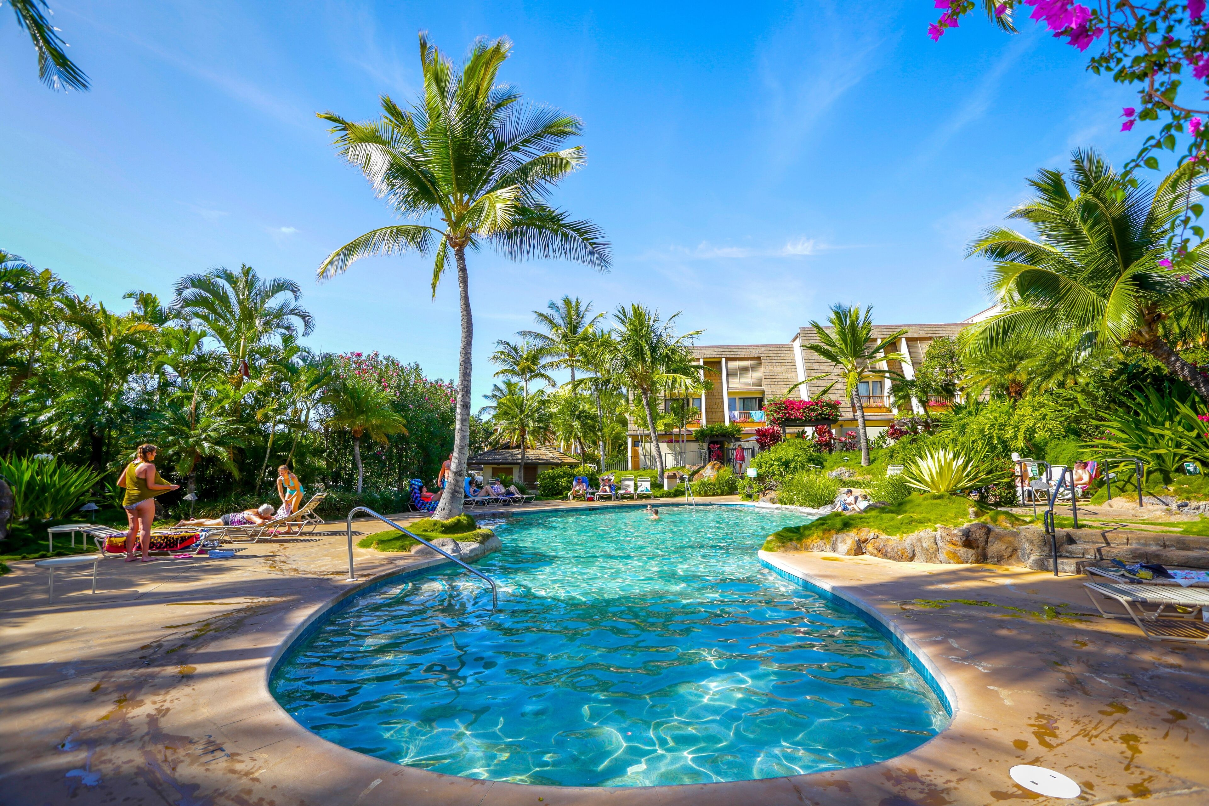 A pool area with lounge chairs, palm trees, and a building in the background.