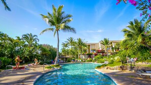 A pool area with lounge chairs, palm trees, and a building in the background.