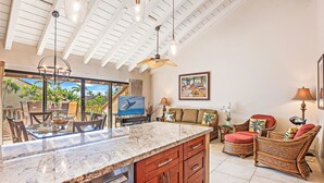 A kitchen with a granite countertop, wooden cabinets, and a dishwasher. There is a dining area with a table and chairs, and a wicker sofa.