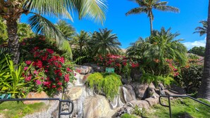 A tropical garden with a waterfall, palm trees, and red flowers.