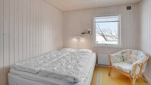 A bedroom with a bed, a chair, a window with a view of trees, and a shelf with items. - 3 bedroom gorgeous home in Vordingborg (Vordingborg)