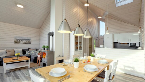 Une salle à manger spacieuse, avec une table en bois dressée pour quatre personnes, entourée de chaises blanches. Une cuisine moderne, avec des armoires blanches et des appareils en acier inoxydable, est visible à l’arrière-plan.