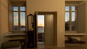 A room with a view of the sea, a bed, a window, and a door leading to a balcony.