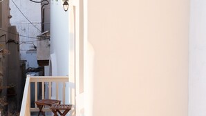 A balcony with a wooden table and chairs, a white railing, and a stone wall in the background.