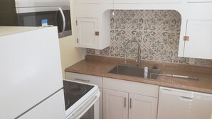 Een kleine keuken met witte kastjes, een roestvrijstalen spoelbak en een magnetron boven het fornuis.