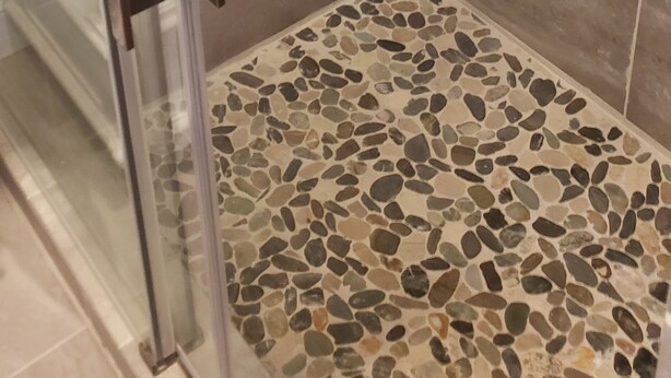 Een douche met een glazen deur, betegelde wanden en een vloer met een kiezelpatroon.