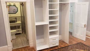 Een inloopkast met open planken en lades, een badkamer met toilet en wastafel, en een deur die naar een andere kamer leidt.