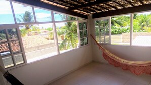 Ein Zimmer mit großen Fenstern, einer Hängematte und Blick auf einen Garten.