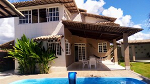 Ein zweistöckiges Haus mit Swimmingpool, überdachter Terrasse und Garten.
