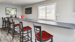 Una cocina con barra, taburetes de bar, una ventana con persianas y un televisor montado en la pared.